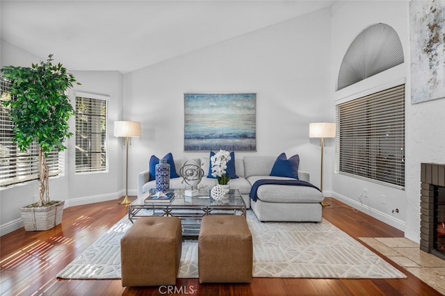 living room with wood-type flooring, lofted ceiling, a brick fireplace, and baseboards