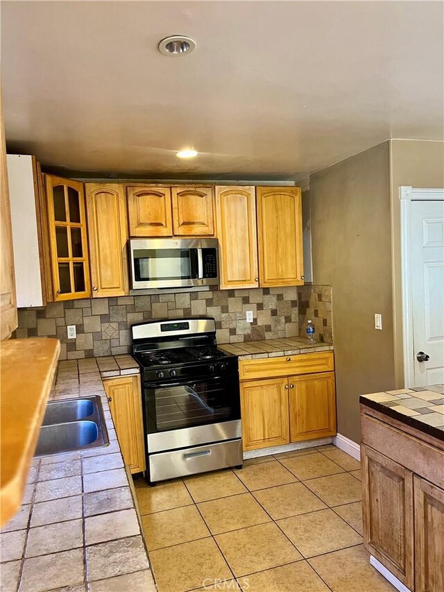 10715 3rd Ave, Hesperia, CA 92345 - kitchen featuring appliances with stainless steel finishes, tile counters, backsplash, glass insert cabinets, and light tile patterned floors