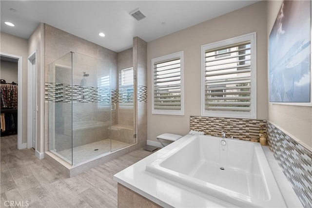 bathroom with a walk in closet, a bath, visible vents, a stall shower, and wood finished floors