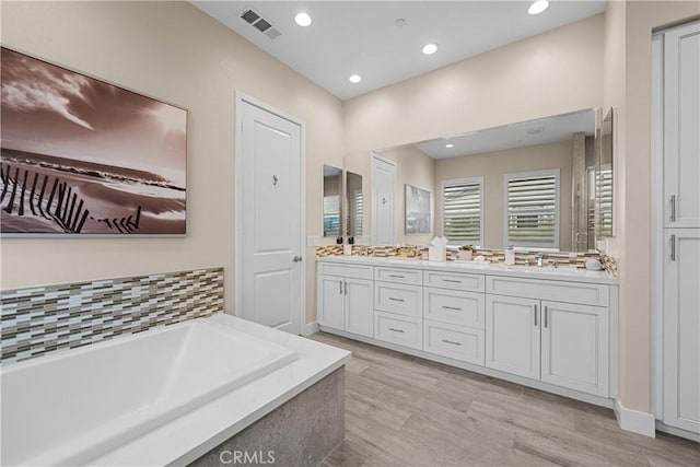 bathroom featuring visible vents, double vanity, recessed lighting, a bath, and a sink