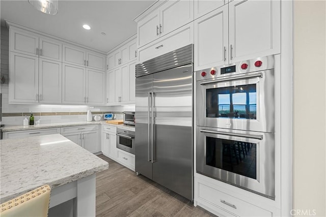 kitchen featuring wood finished floors, recessed lighting, white cabinetry, light stone counters, and appliances with stainless steel finishes