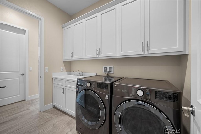 clothes washing area featuring cabinet space, a sink, baseboards, light wood-style floors, and separate washer and dryer
