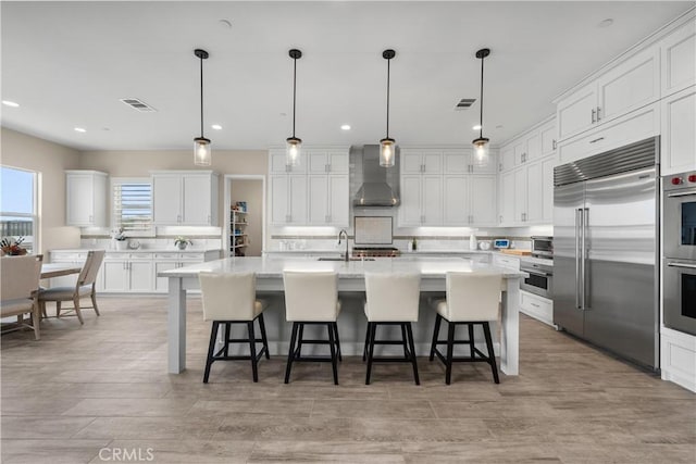 kitchen featuring visible vents, white cabinetry, appliances with stainless steel finishes, and wall chimney range hood