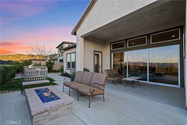 patio terrace at dusk featuring fence and an outdoor living space with a fire pit
