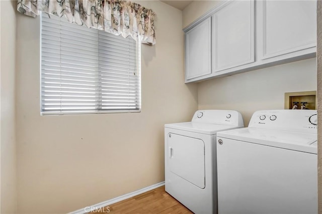 laundry room with baseboards, washing machine and dryer, cabinet space, and light wood-type flooring