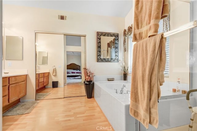 full bathroom with vanity, a garden tub, wood finished floors, ensuite bathroom, and visible vents