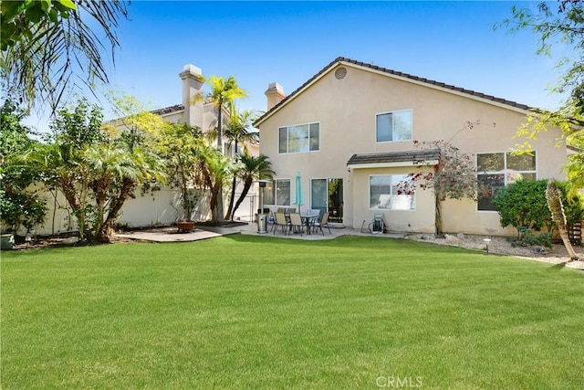 rear view of property with stucco siding, fence, a lawn, and a patio