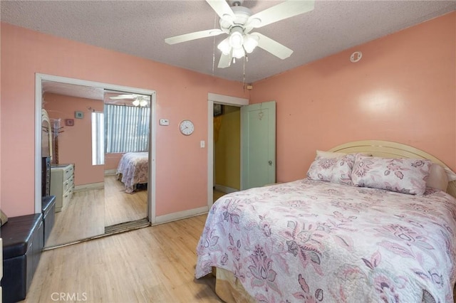 bedroom featuring light wood-style flooring, a textured ceiling, baseboards, and ceiling fan