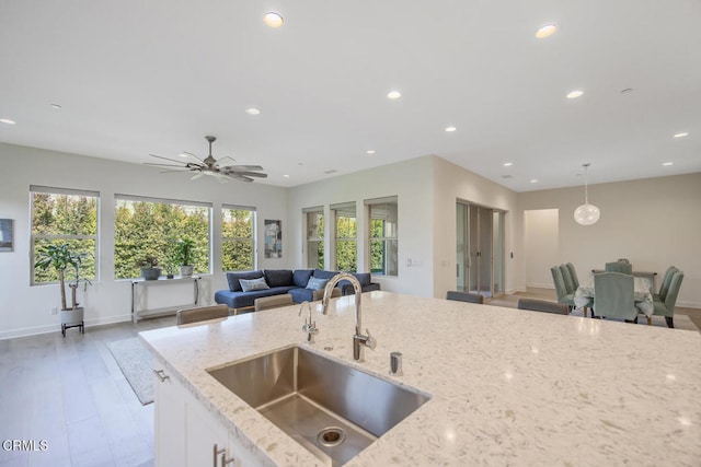 kitchen featuring open floor plan, light stone countertops, a sink, and recessed lighting