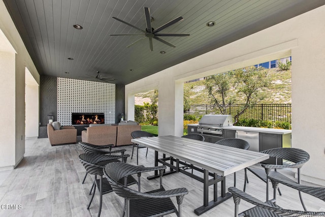 view of patio / terrace featuring exterior kitchen, area for grilling, fence, outdoor dining space, and ceiling fan