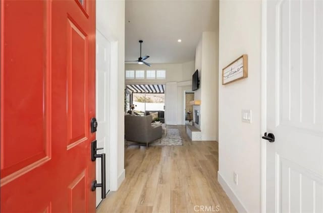 entryway with a fireplace, ceiling fan, baseboards, and light wood-type flooring