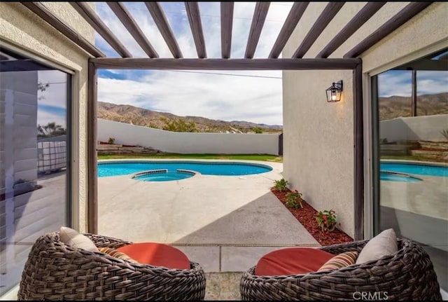 view of swimming pool with fence, a mountain view, a pool with connected hot tub, and a patio area