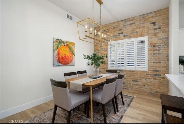 dining space with baseboards, brick wall, visible vents, a notable chandelier, and wood finished floors