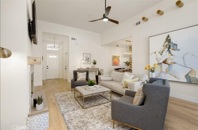 living area featuring ceiling fan with notable chandelier, visible vents, wood finished floors, and baseboards