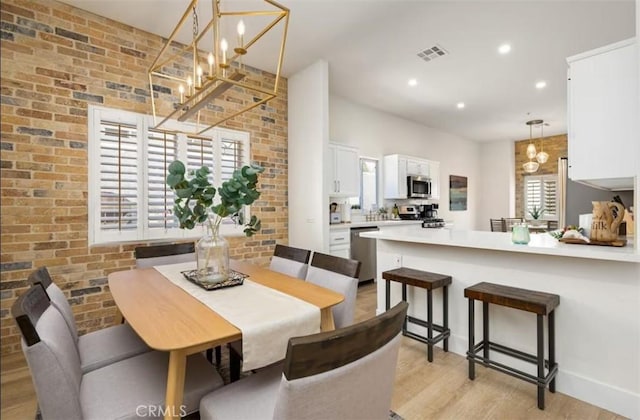 dining space with a chandelier, brick wall, light wood finished floors, and visible vents