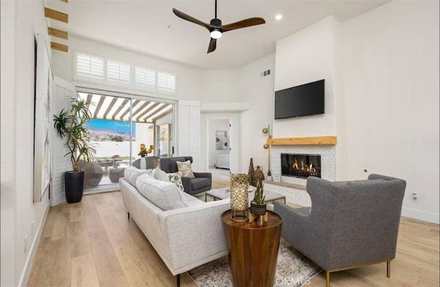 living area with a tiled fireplace, baseboards, light wood-style floors, and ceiling fan