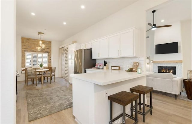 kitchen featuring white cabinets, light wood-type flooring, open floor plan, backsplash, and freestanding refrigerator