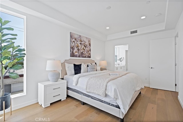 bedroom with a raised ceiling, light wood-type flooring, baseboards, visible vents, and recessed lighting