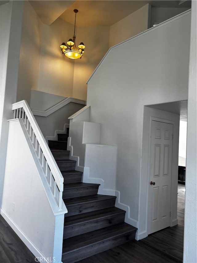 staircase with baseboards, wood finished floors, and an inviting chandelier