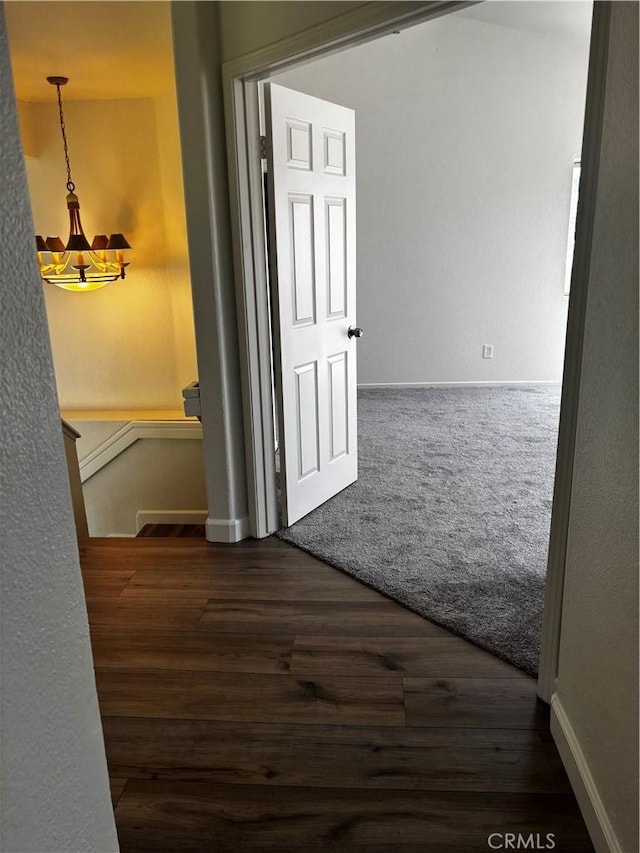 hallway featuring baseboards, an upstairs landing, dark wood-style floors, and an inviting chandelier