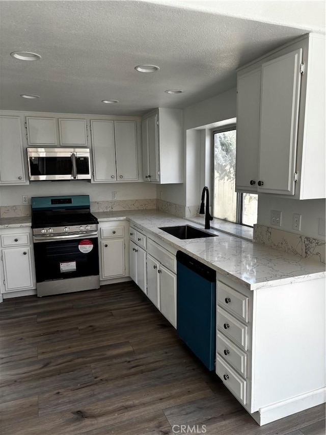 kitchen featuring a textured ceiling, light stone countertops, stainless steel appliances, a sink, and dark wood-style floors