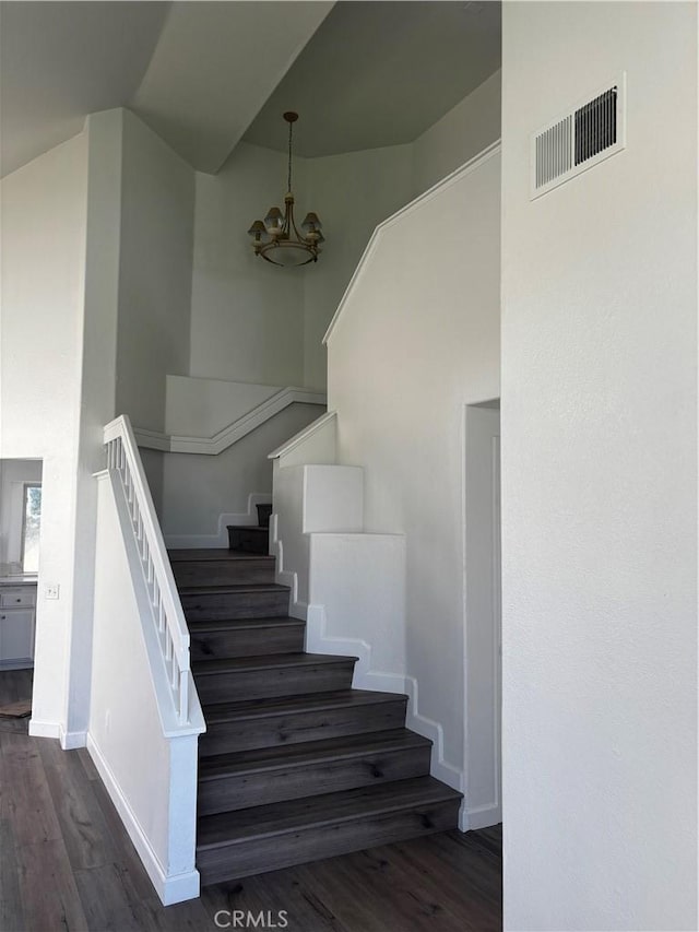 stairway featuring baseboards, visible vents, wood finished floors, and a chandelier