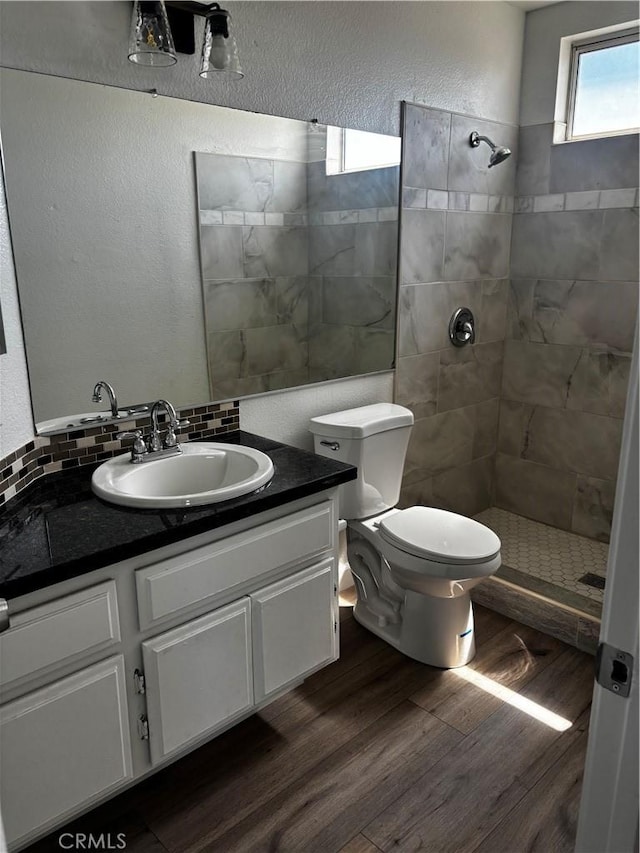 full bath featuring vanity, wood finished floors, toilet, and tiled shower
