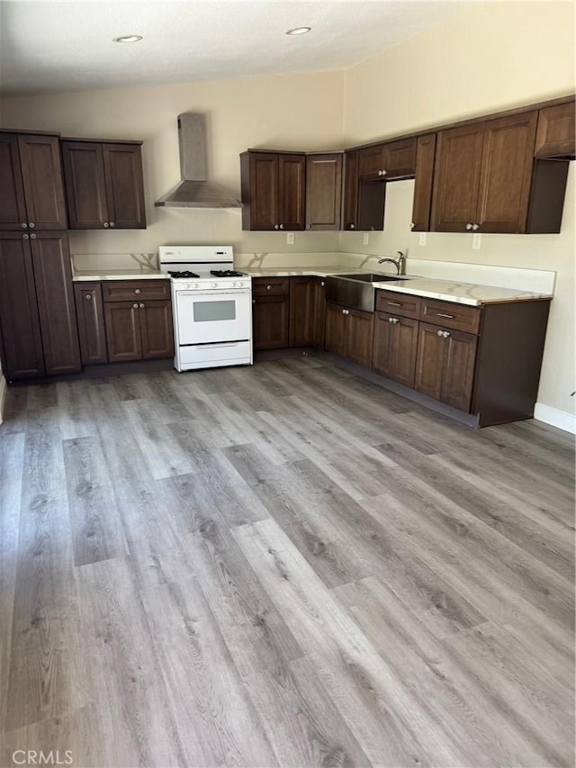 518 E 2nd St, Rialto, CA 92376 - kitchen with white gas range oven, wall chimney exhaust hood, light countertops, light wood finished floors, and dark brown cabinets