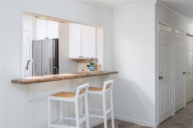 kitchen featuring crown molding, a breakfast bar, freestanding refrigerator, white cabinetry, and tasteful backsplash