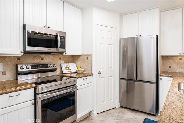 kitchen featuring white cabinets, stainless steel appliances, light stone counters, and decorative backsplash