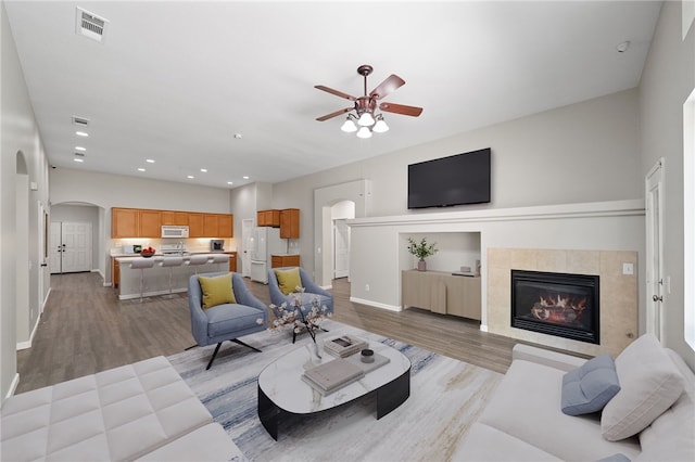 24898 Sunset Vista Ave, Menifee, CA 92584 - living area with arched walkways, light wood-style floors, a ceiling fan, baseboards, and a tiled fireplace