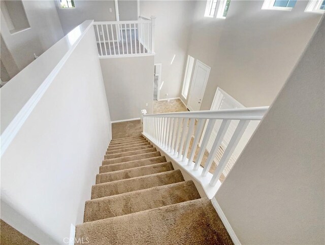 stairs featuring baseboards, a towering ceiling, and carpet flooring