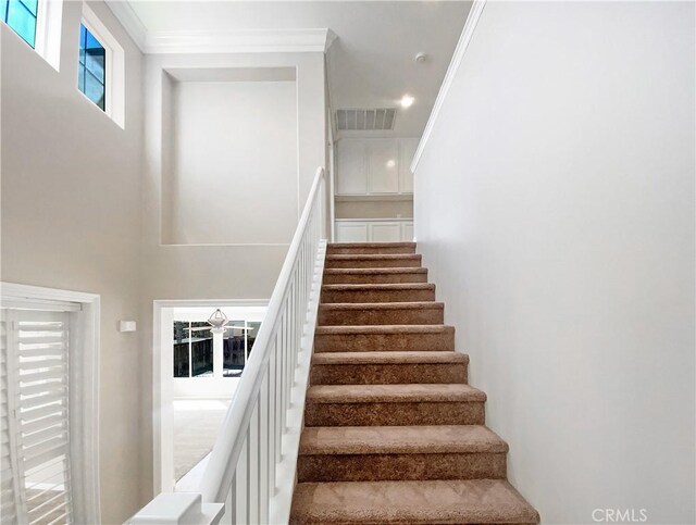 staircase featuring a high ceiling, visible vents, and crown molding