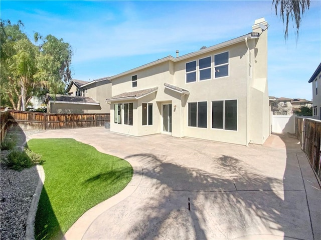 rear view of property with a fenced backyard, a lawn, stucco siding, and a patio