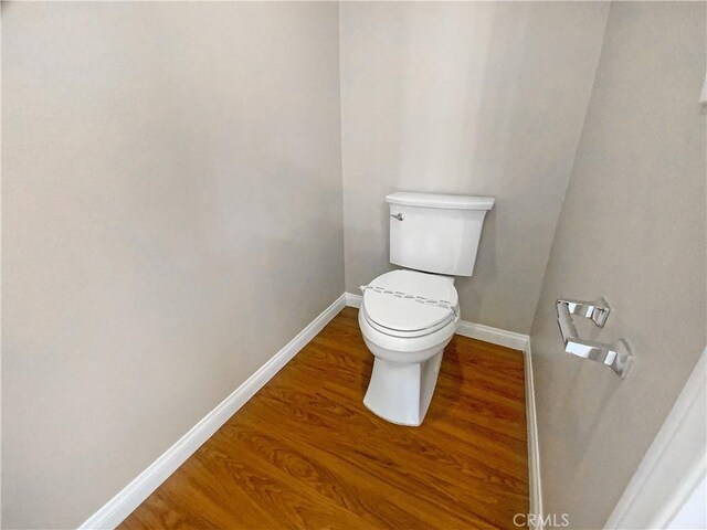 bathroom featuring baseboards, wood finished floors, and toilet