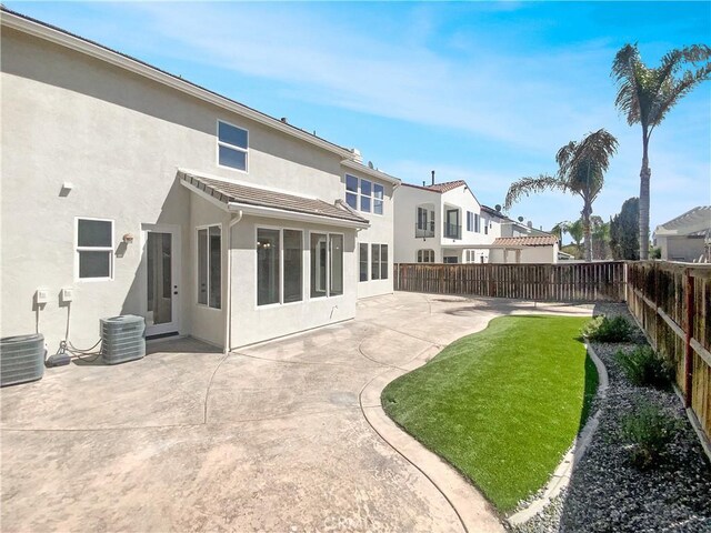 rear view of house featuring a tile roof, stucco siding, a fenced backyard, a yard, and a patio area