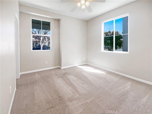 carpeted spare room with a ceiling fan and baseboards