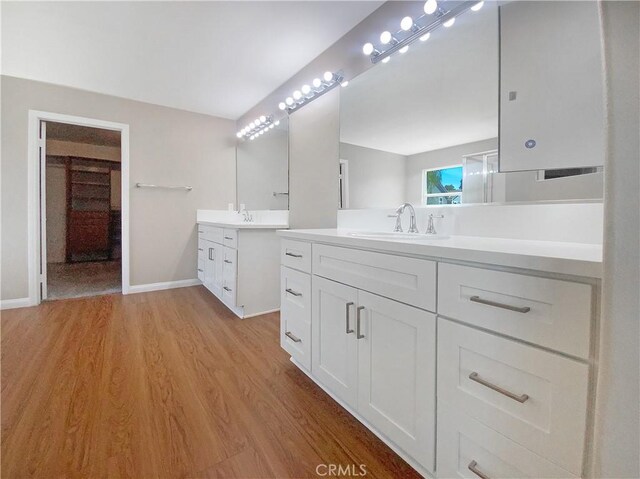 bathroom with baseboards, wood finished floors, a sink, and two vanities