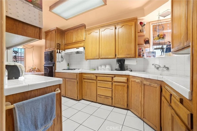 kitchen with light tile patterned floors, black appliances, under cabinet range hood, and decorative backsplash