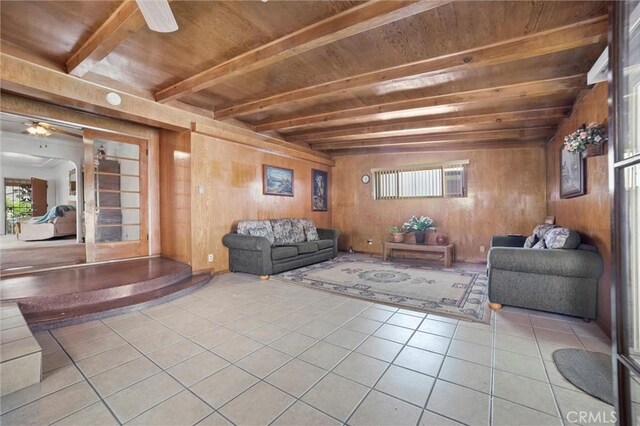 tiled living area featuring wood walls, beamed ceiling, a ceiling fan, and wood ceiling