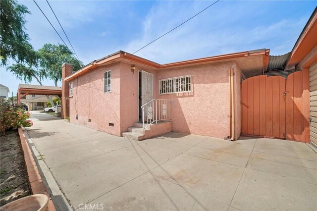 back of house featuring a chimney, stucco siding, a gate, a carport, and crawl space