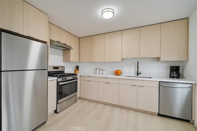 kitchen featuring light brown cabinetry, under cabinet range hood, a sink, and stainless steel appliances
