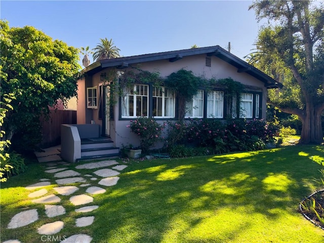 bungalow featuring stucco siding, fence, and a front lawn