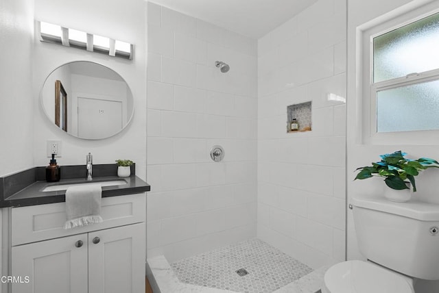 full bathroom with toilet, tiled shower, and vanity
