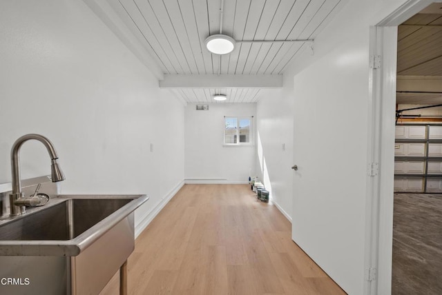 interior space featuring light wood finished floors, baseboards, a sink, and beam ceiling
