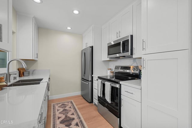 kitchen featuring stainless steel appliances, light wood-type flooring, white cabinetry, and a sink