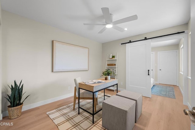 office space with light wood-style flooring, a ceiling fan, a barn door, and baseboards