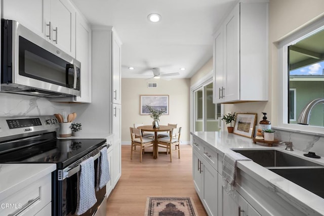 kitchen featuring tasteful backsplash, a sink, a ceiling fan, stainless steel appliances, and light wood-style flooring