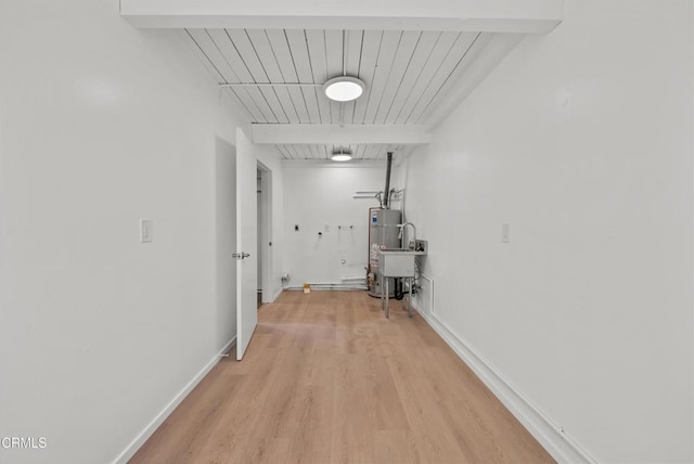 corridor with light wood finished floors, baseboards, beamed ceiling, and gas water heater