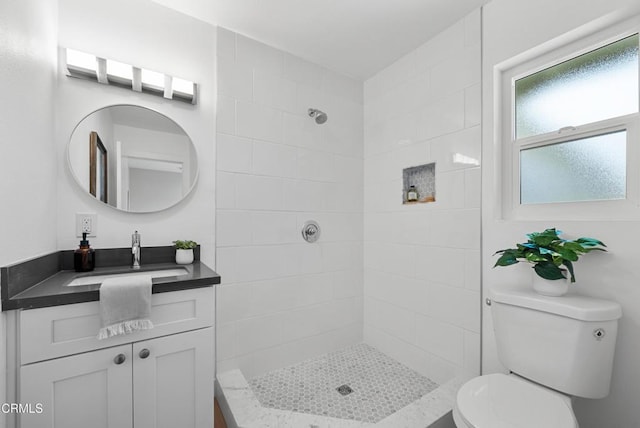 bathroom with toilet, tiled shower, and vanity
